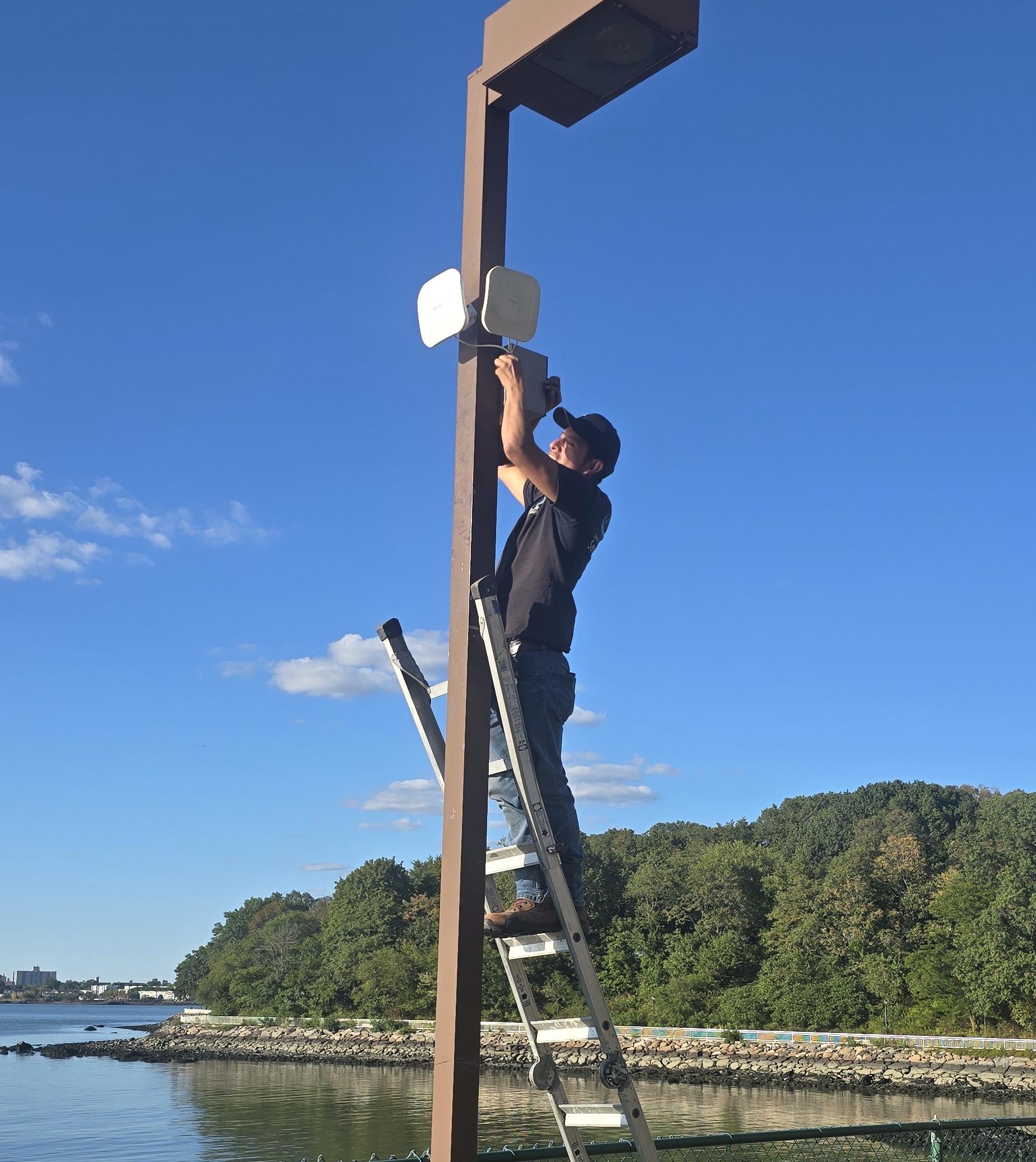 Technician installing outdoor wireless bridge access point on a light pole by the waterfront